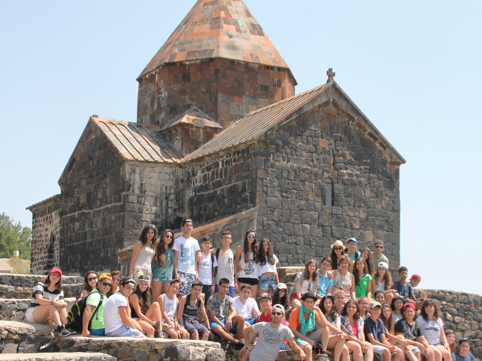 Participants of AGBU Discover Armenia Program sitting in rows outside an old Armenian monastery.