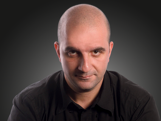 A bald young man looking straight to the camera on a dark background